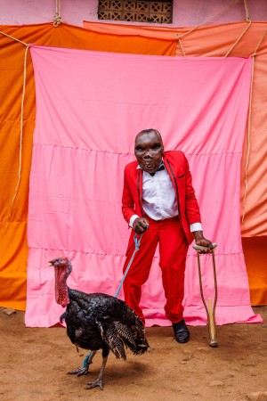 Man with a physical disability standing in front of a colourful bacldrop, holding a turkey on a leash. 