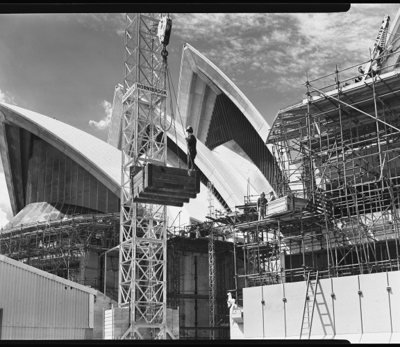 Black and white photograph from 1971, showing construction of Sydney Opera House, including a crane with the Hornibrook logo in the foreground.