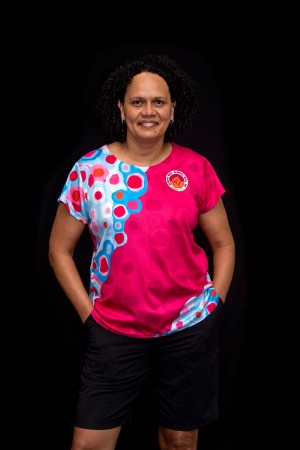 woman smiling at the camera wearing a pink Indigenous shirt.