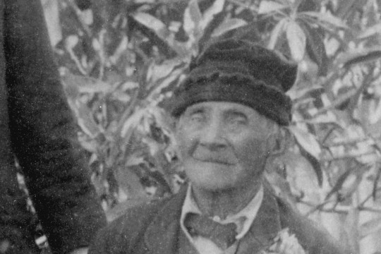 Portrait of elderly man in a suit wearing a knitted hat, sitting on a chair in the garden