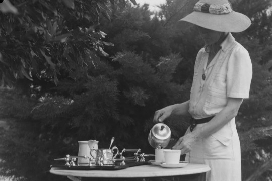 Woman standing at small table in backyard pouring tea, 1910-1954, Arthur McLeod, Brisbane John Oxley Library, State Library of Queensland, Image number:32086-0008-0003.