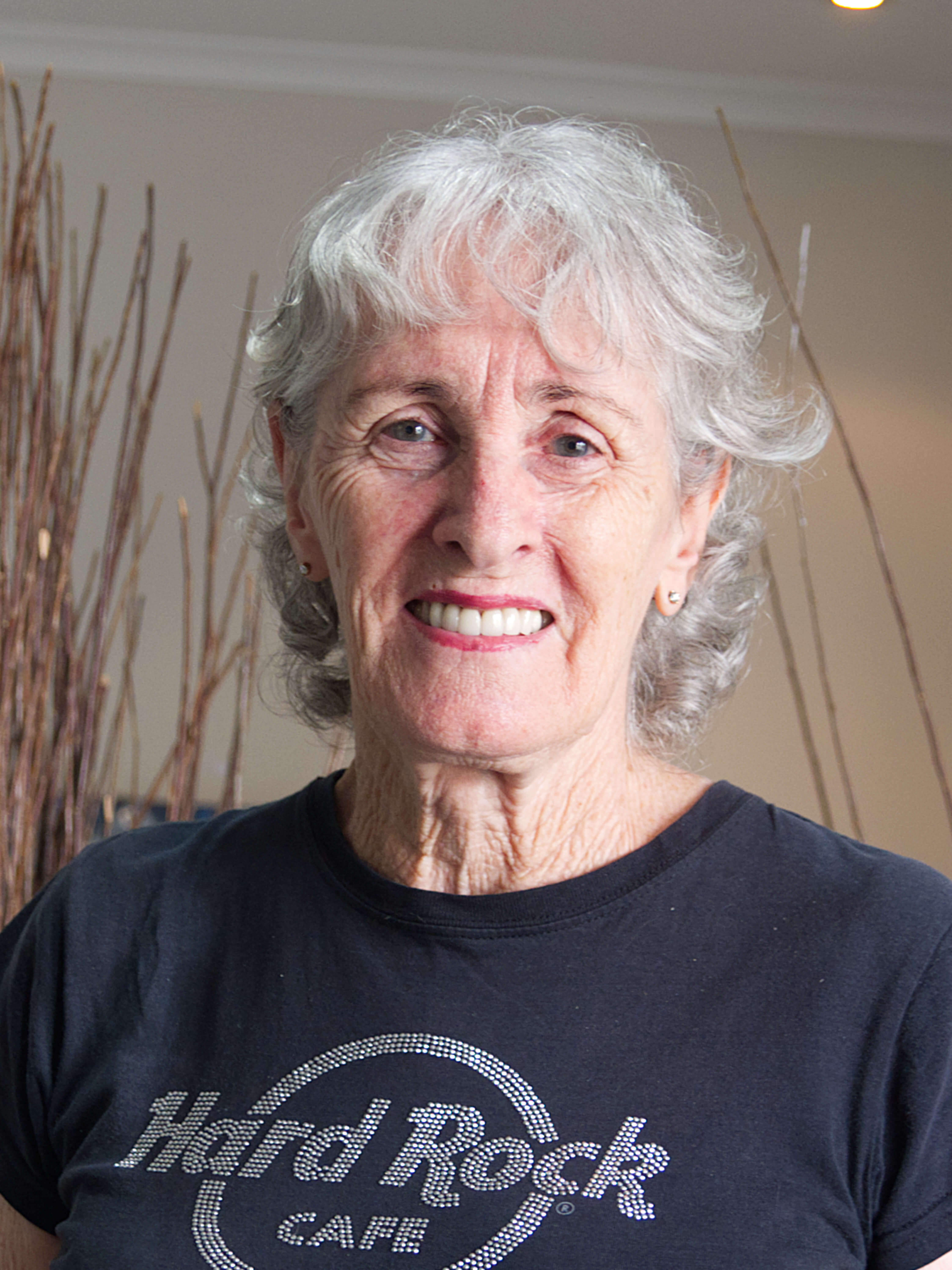 photographic portrait of a woman with short grey hair, blue eyes and red lipstick, she is wearing stud earrings, and wearing a black T-shirt saying Hard Rock Cafe