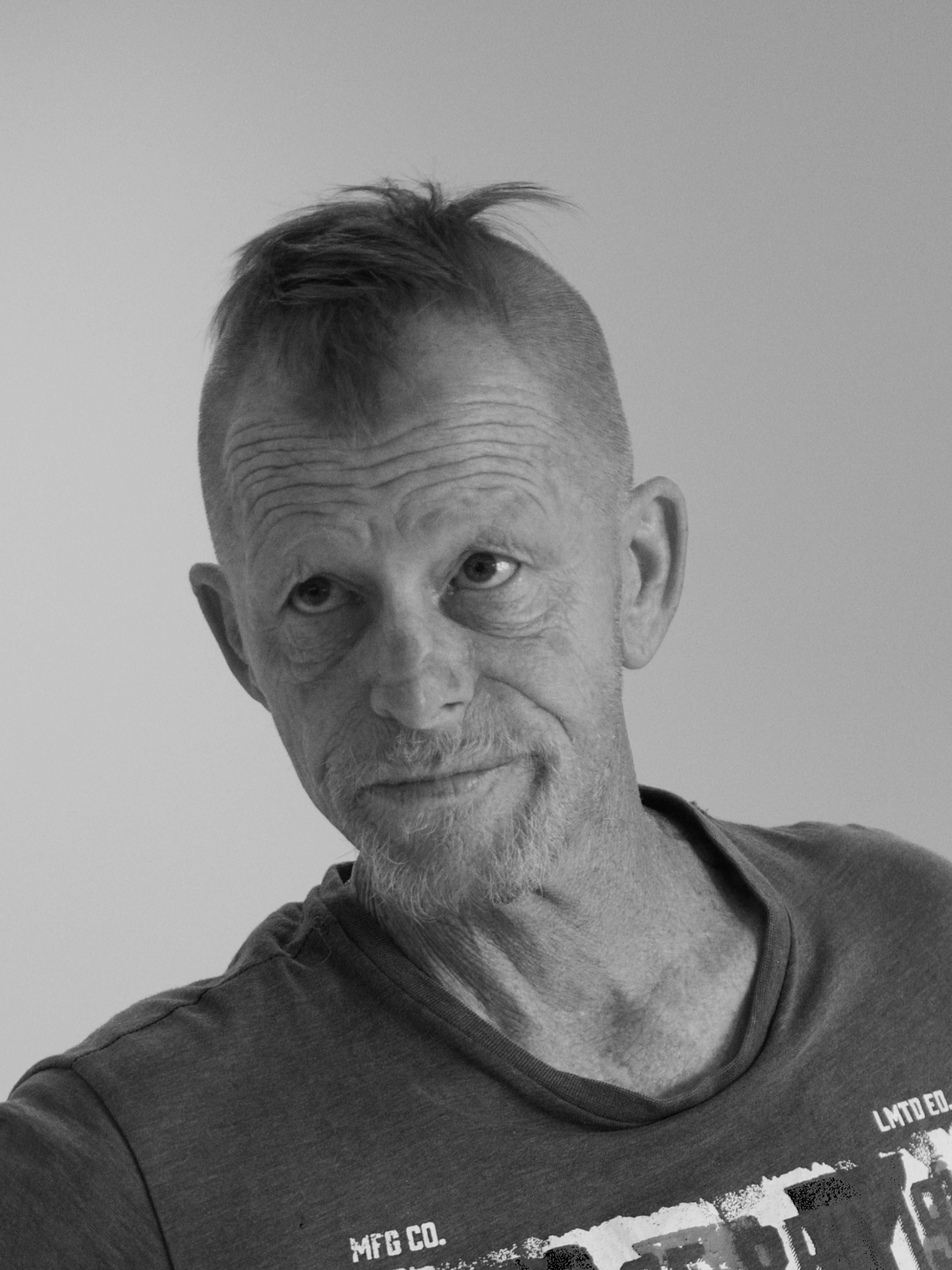 black and white portrait of a middle aged man looking up, he has shaved sides of his head, he is wearing a t-shirt with white writing