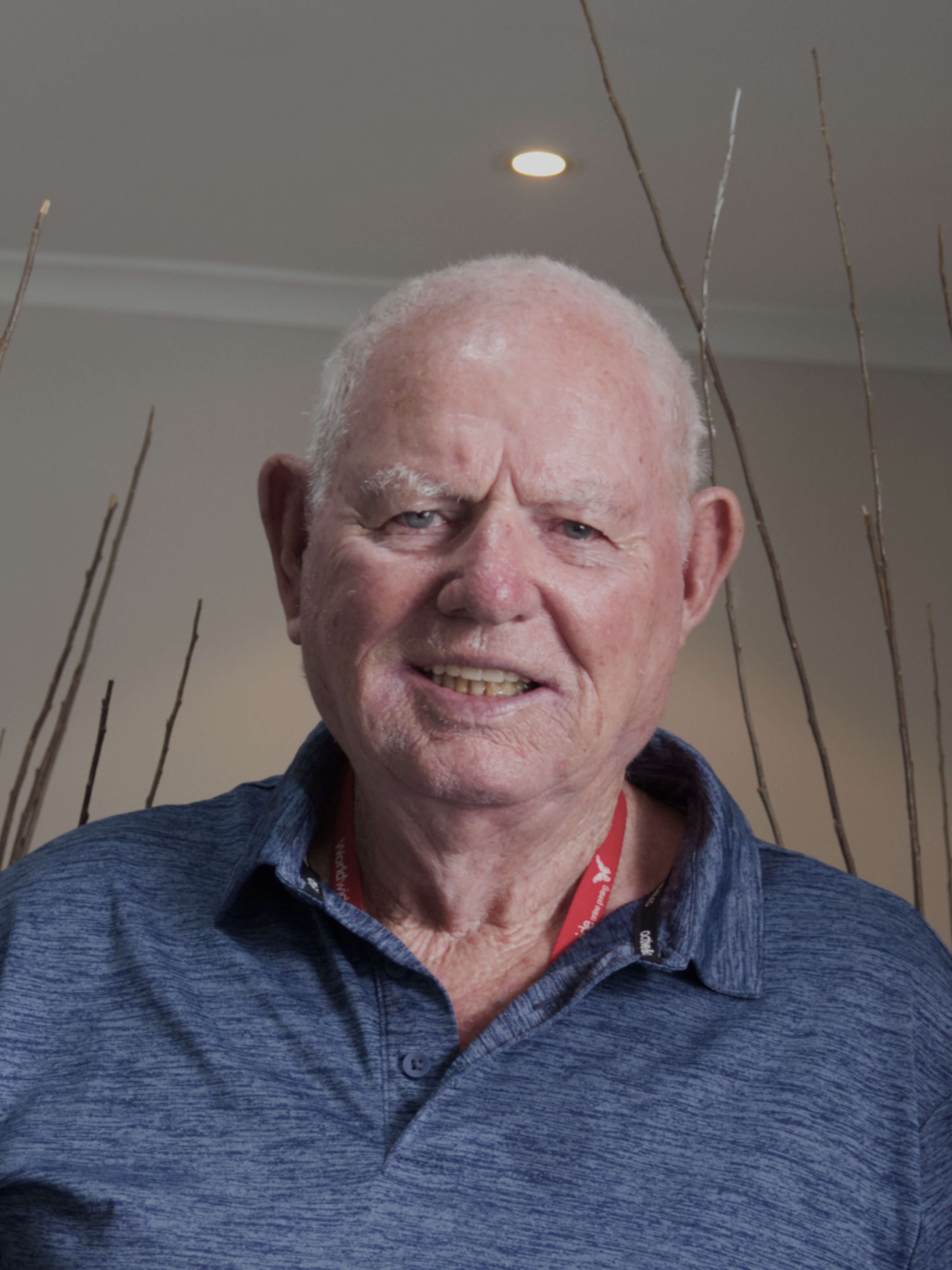 photographic portrait of Brian Laing, a older man with white hair and blue eyes smiling at the camera, we wears a blue collared shirt