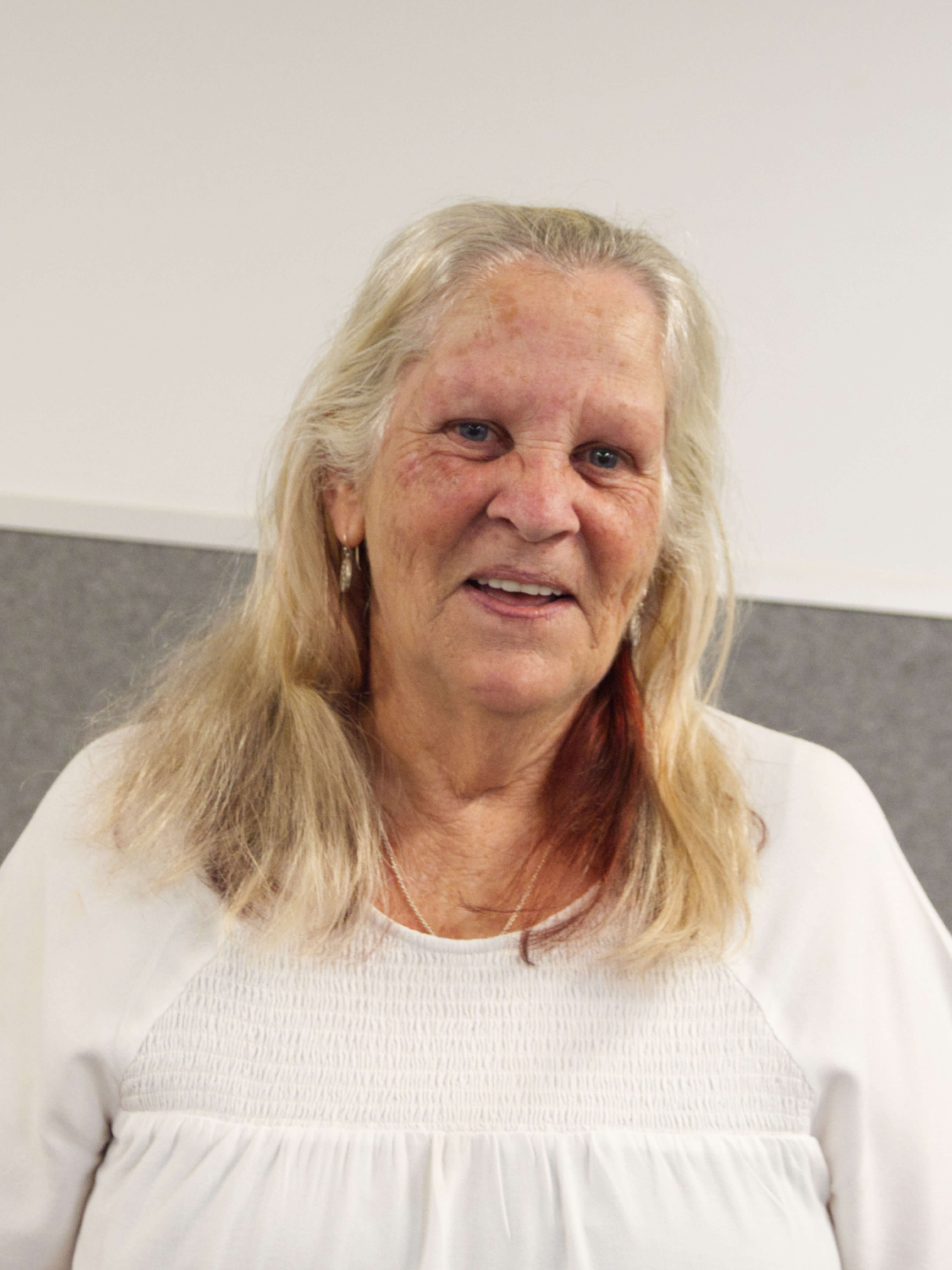 photographic portrait of Marcia Lebrocq, a middle aged woman with blonde hair wearing a white shirt with gold earrings and necklace