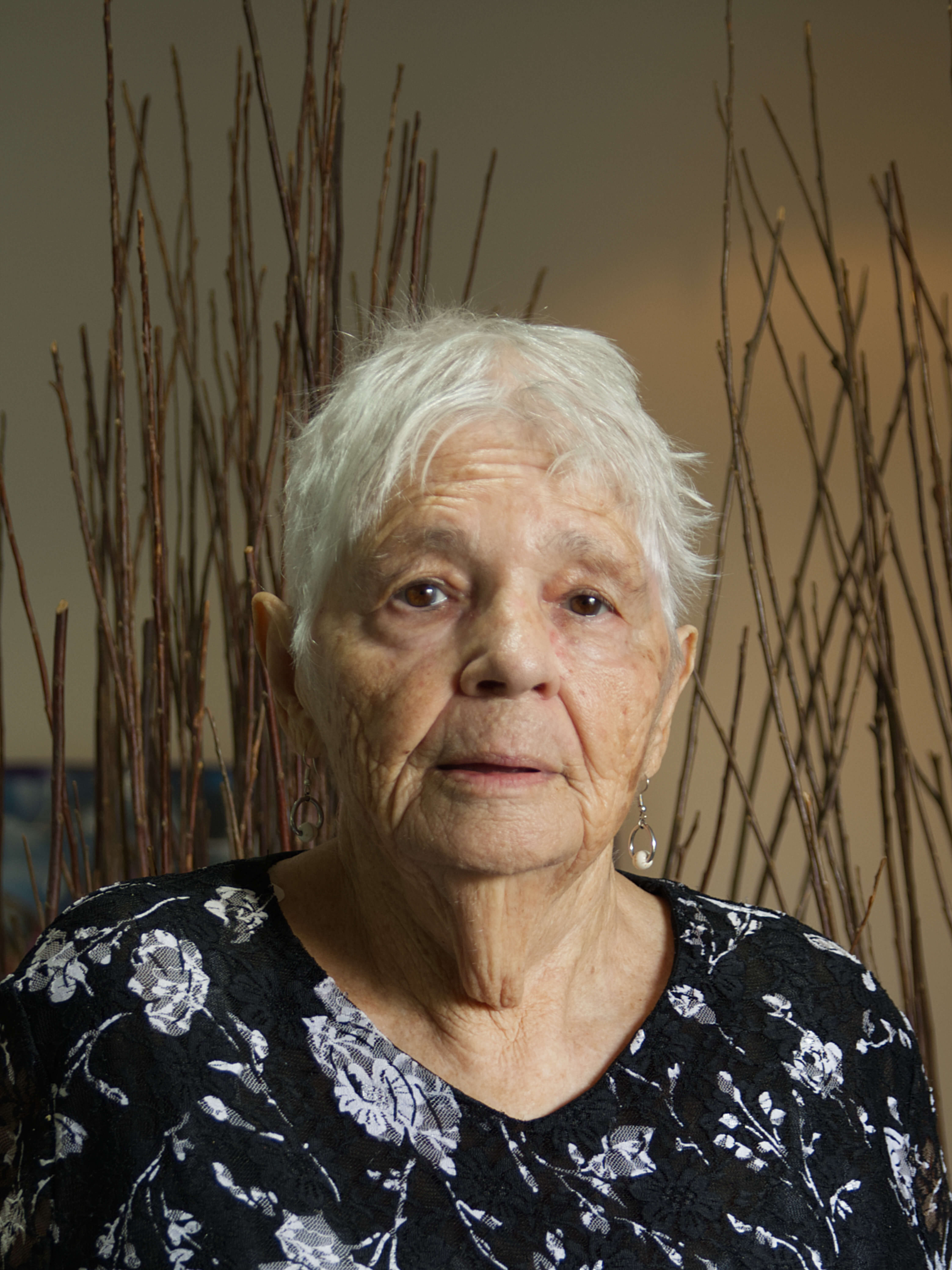 photographic portrait of Mary Mason, a older woman with short white hair looking directly at the camera, wearing a black shirt with white flowers