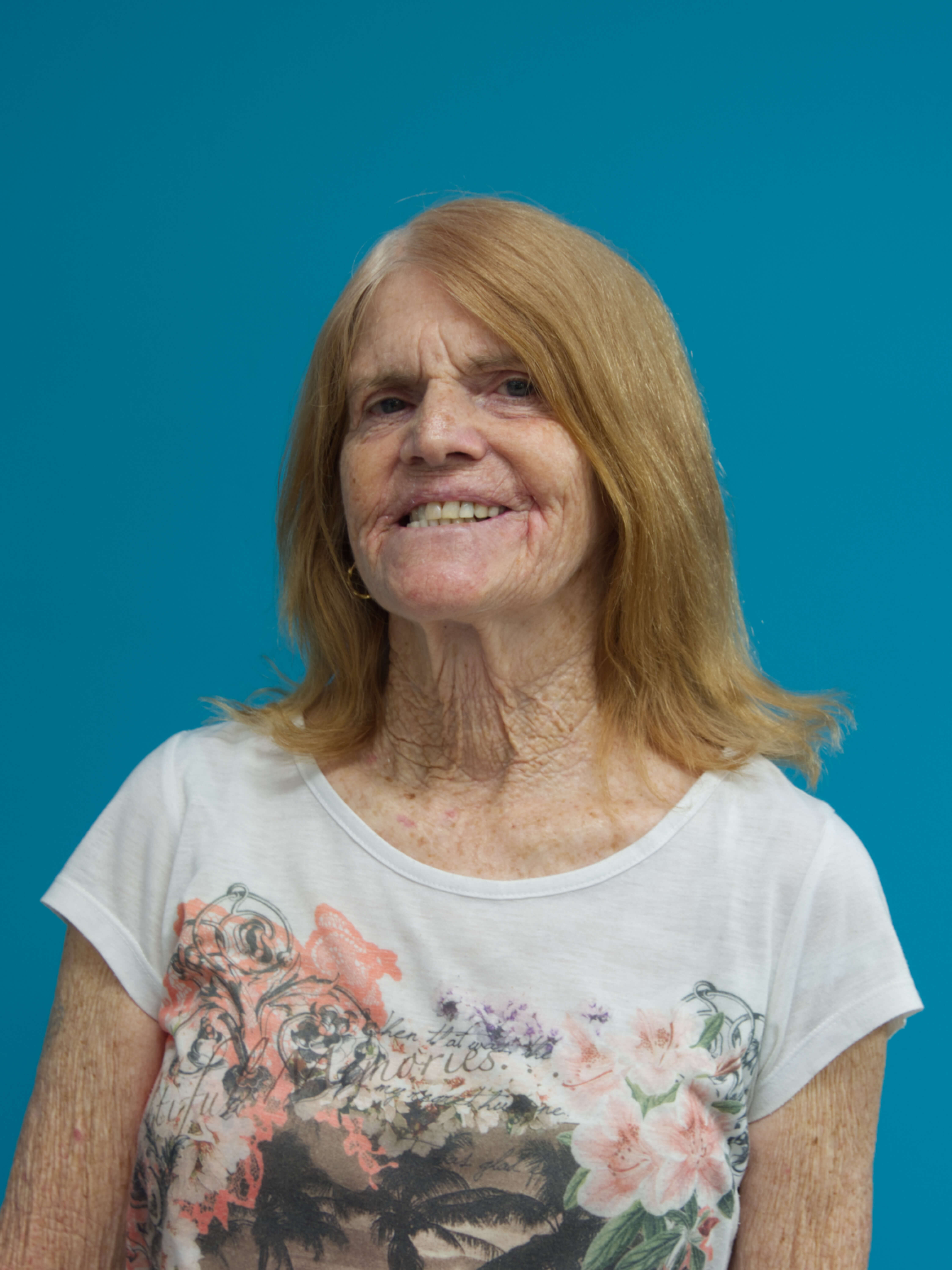 photographic portrait of Sherryl munson, older woman with red hair shoulder length, smiling at the camera, wearing a whiite t-shirt with flowers