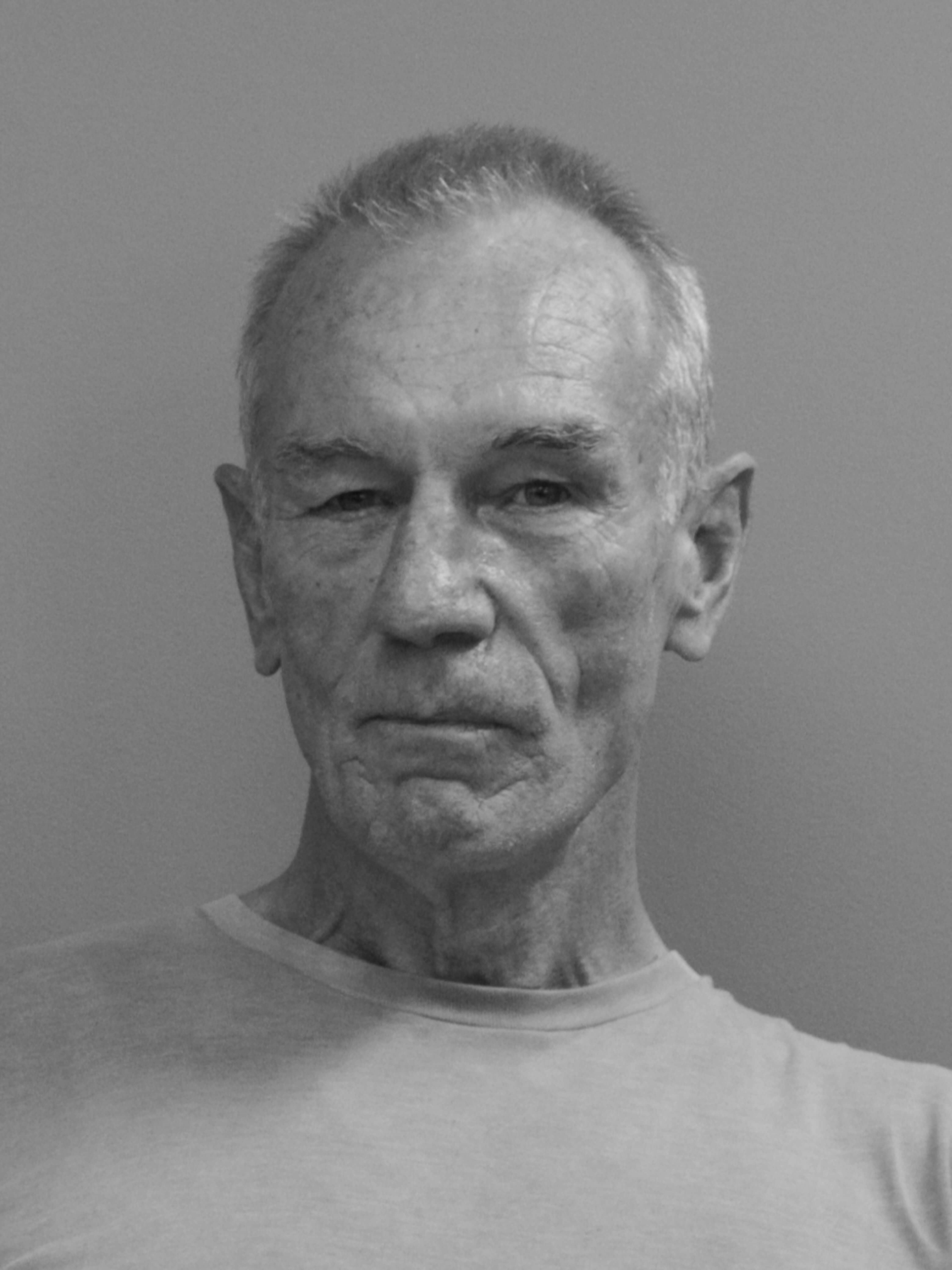 black and white photographic portrait of Des Murray, a older man with shirt grey hair, looking directly at the camera with an serious expression