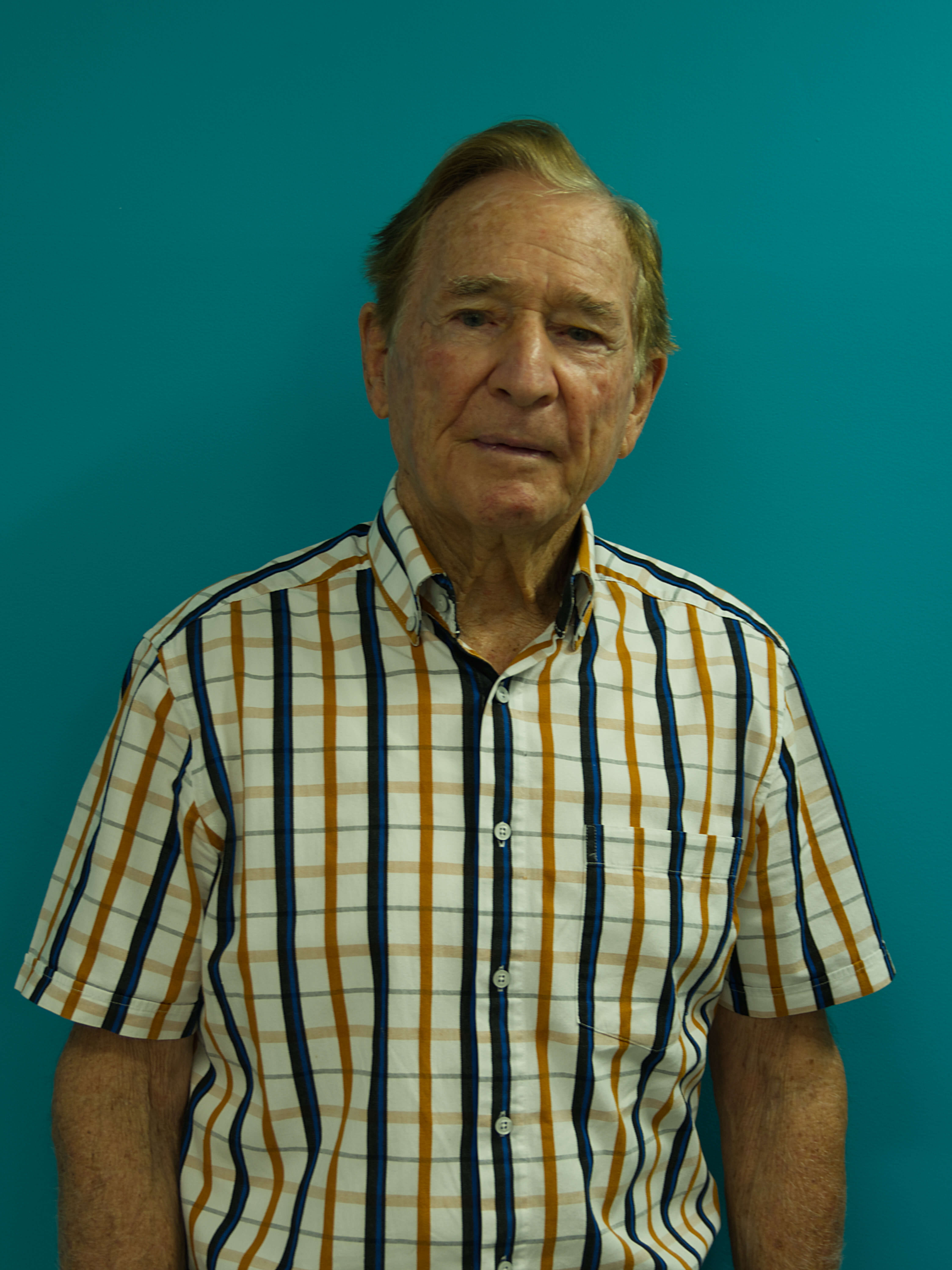 photographic portrait of Russel Willis, a older man with short grey hair wearing a yellow white and blue striped collared shirt