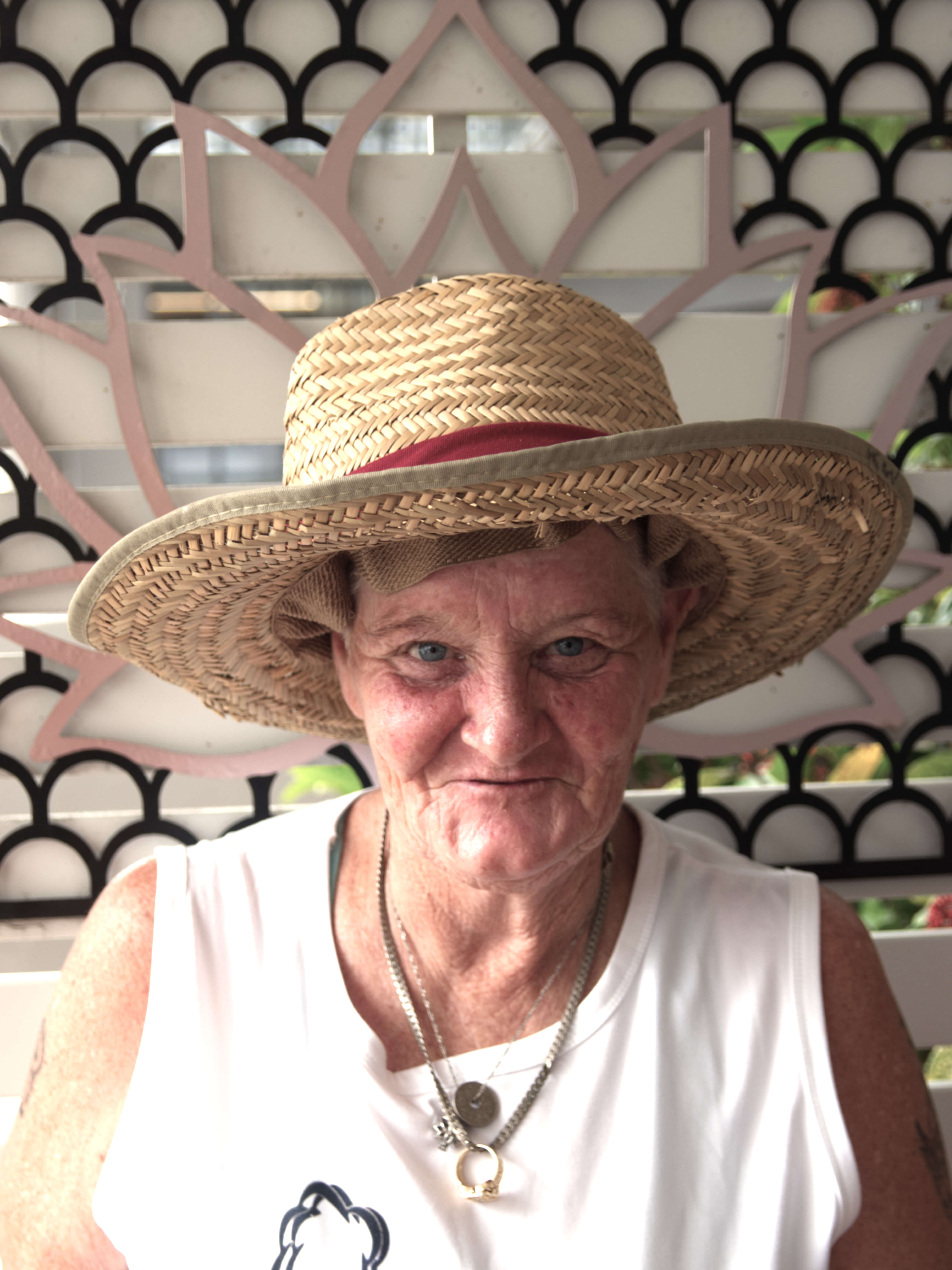 photographic portrait of Kattrina Wood, she is wearing a broad brim straw hat with a red band, she has a white sleeveless shirt and silver necklaces