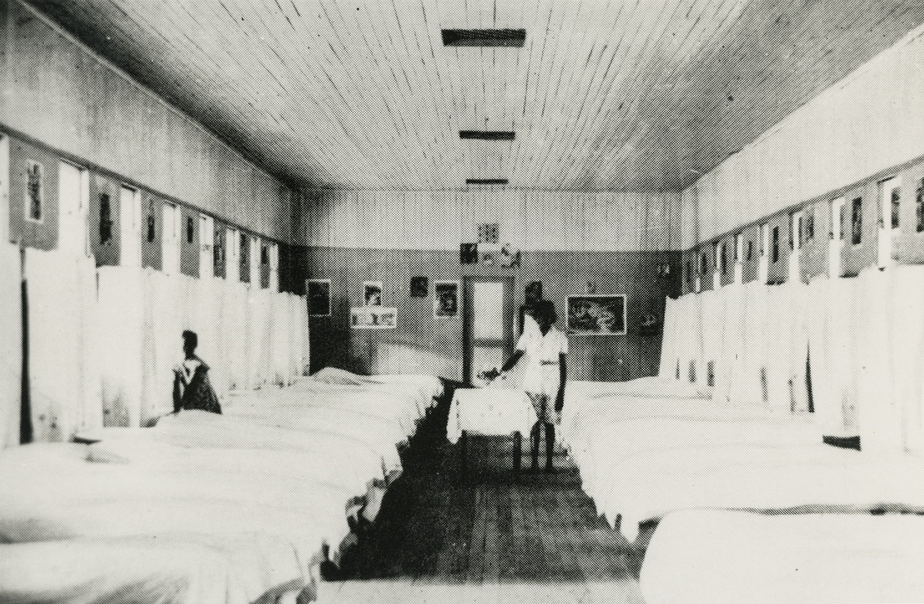 Black and white image of single beds in two rows against a wall.
