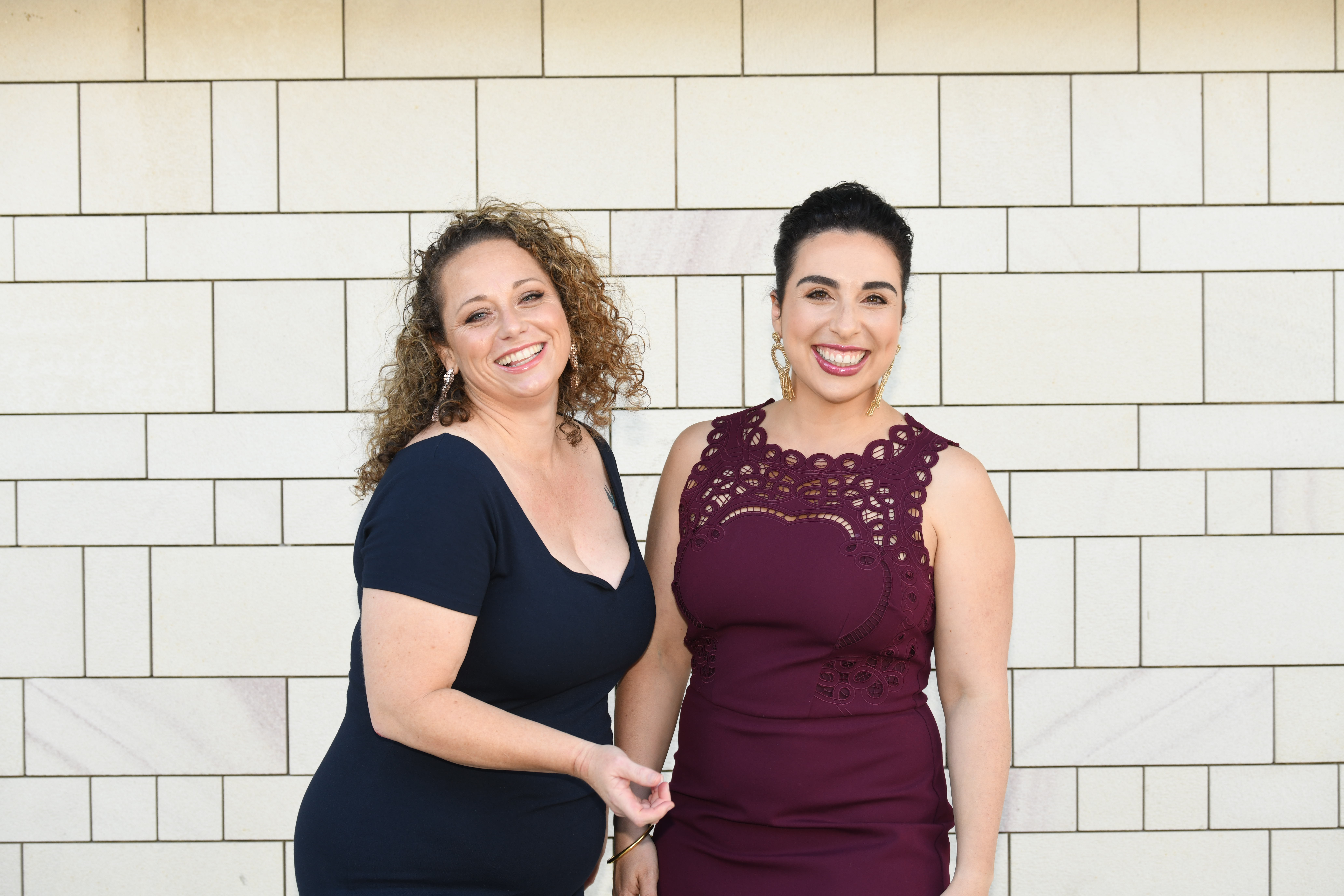 Like A Photon Creative Kristen Souvlis and Nadine Bates from Like A Photon Creative standing together in front of a white brick wall and smiling at the camera