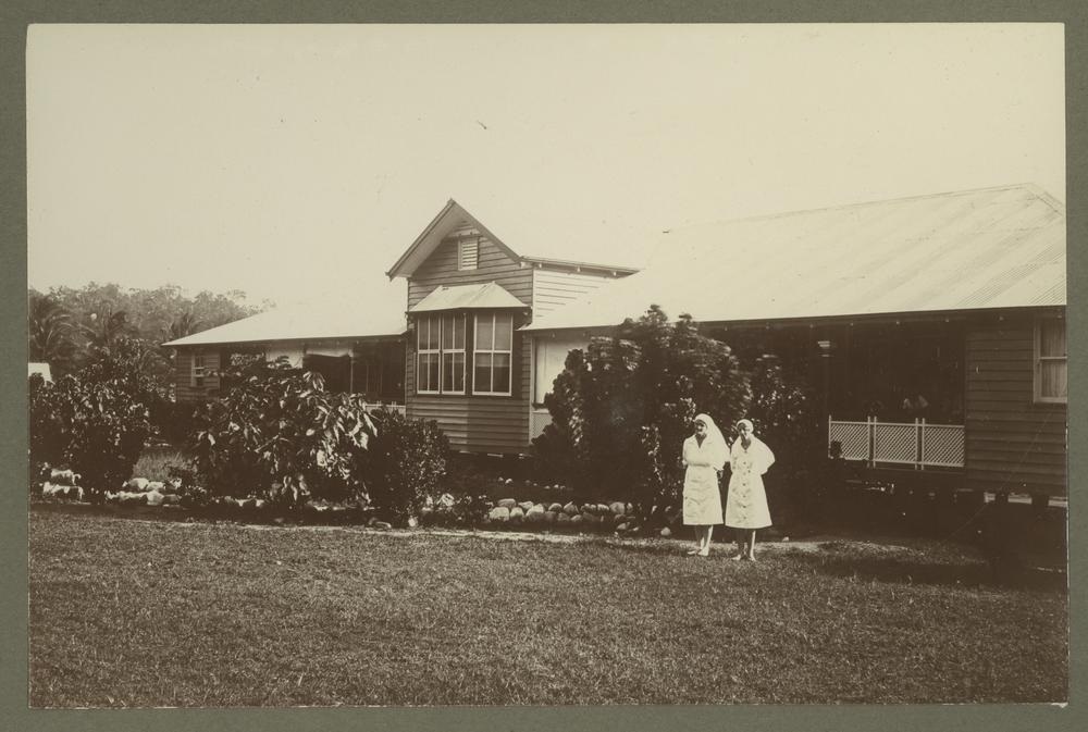 Matron Collins and Sister Gumley, two women dressed in white nun outfits, stand in front of a clinic building
