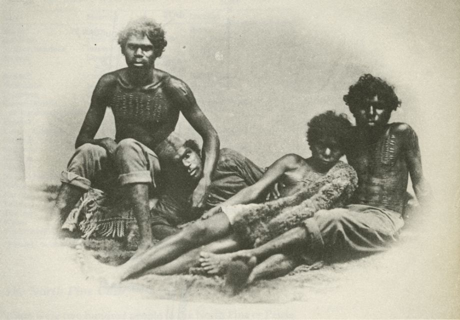 Studio portrait of unnamed Aboriginal people in George Street, Brisbane with a possum skin cloak covering the woman.