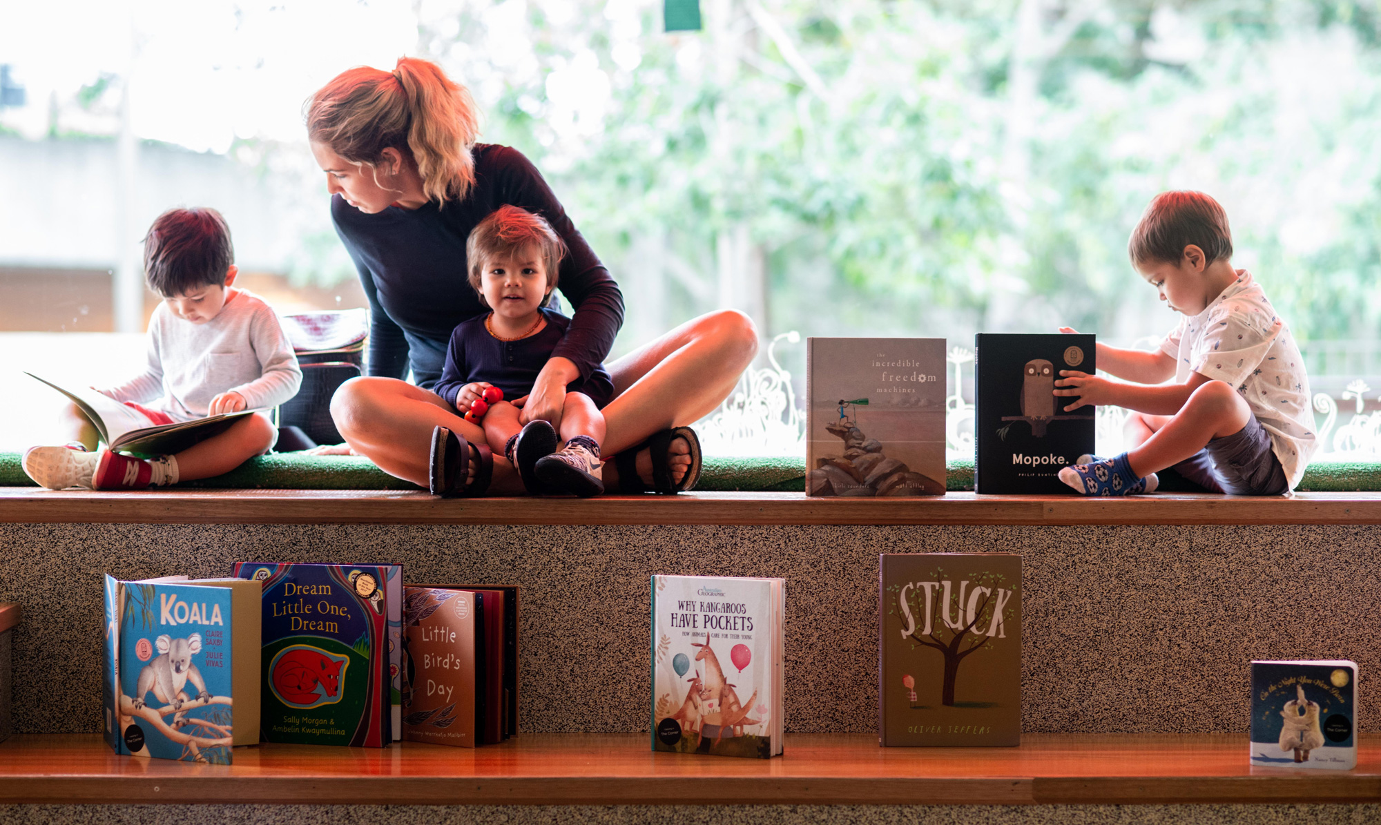 3 children with 1 adult lady in the corner looking at books