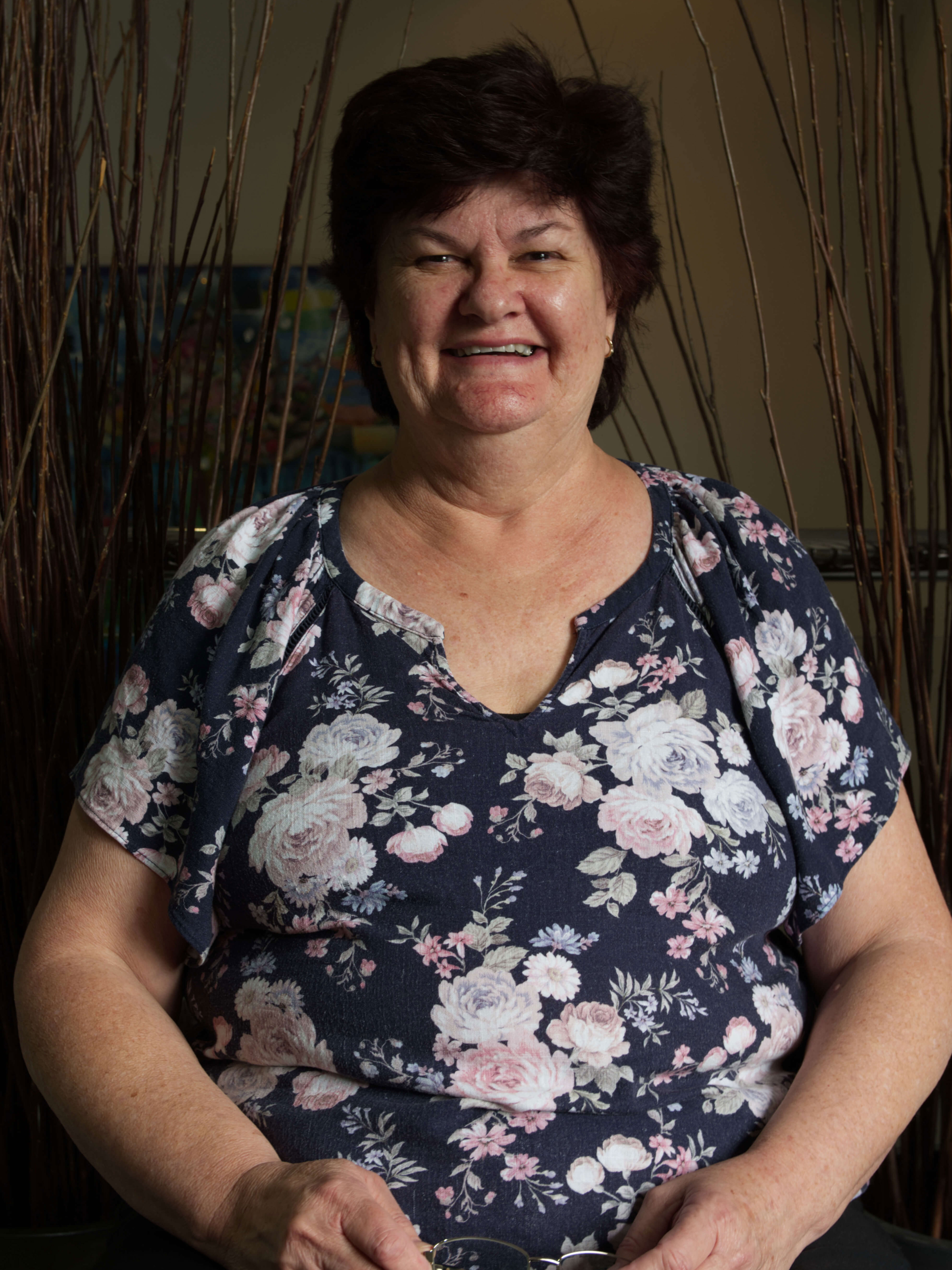 photographic portrait of a woman smiling at the camera, with short brown hair and a dark blue shirt with white and pink flowers
