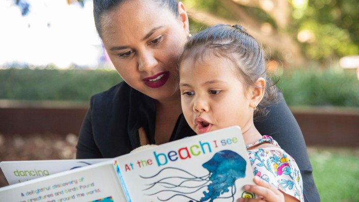 Woman reading a book to a child in an outdoor area
