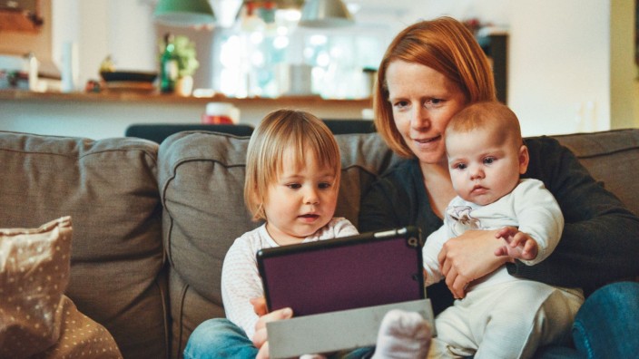 Mother and two young children sitting on a chair looking at an ipad