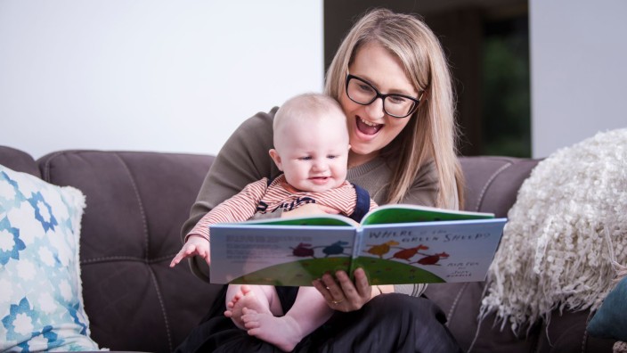 Woman sitting at home reading a book with her baby