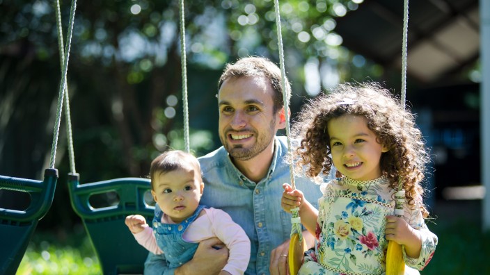 Father and daughters playing on swing set