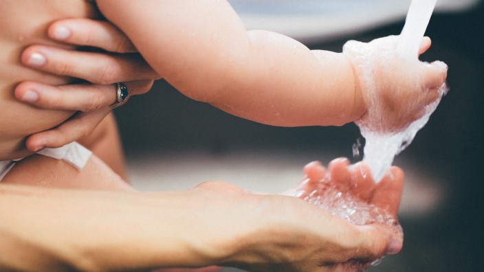 Two hands are under a running tap - a baby hand and an adult hand