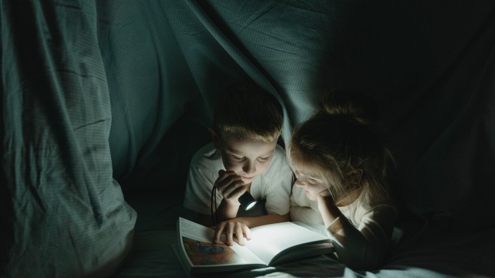 Brother and sister looking at book in torch light