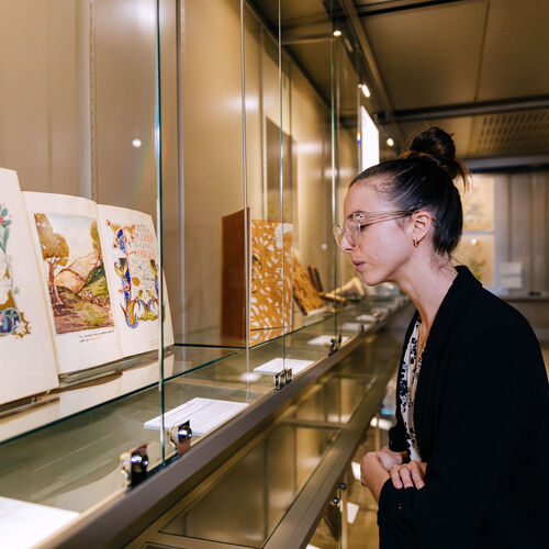 Woman looking at old illustrated book behind a glass cabinet.
