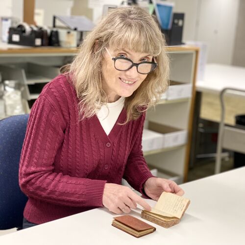 Woman with long blonde hair and glasses in red cardigan reading old diaries