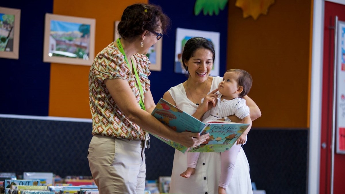 Mother and baby looking at books inside library with a librarian