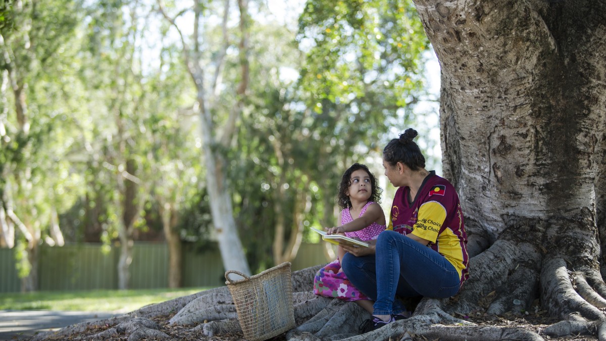 Mother and daughter reading a book under a tree