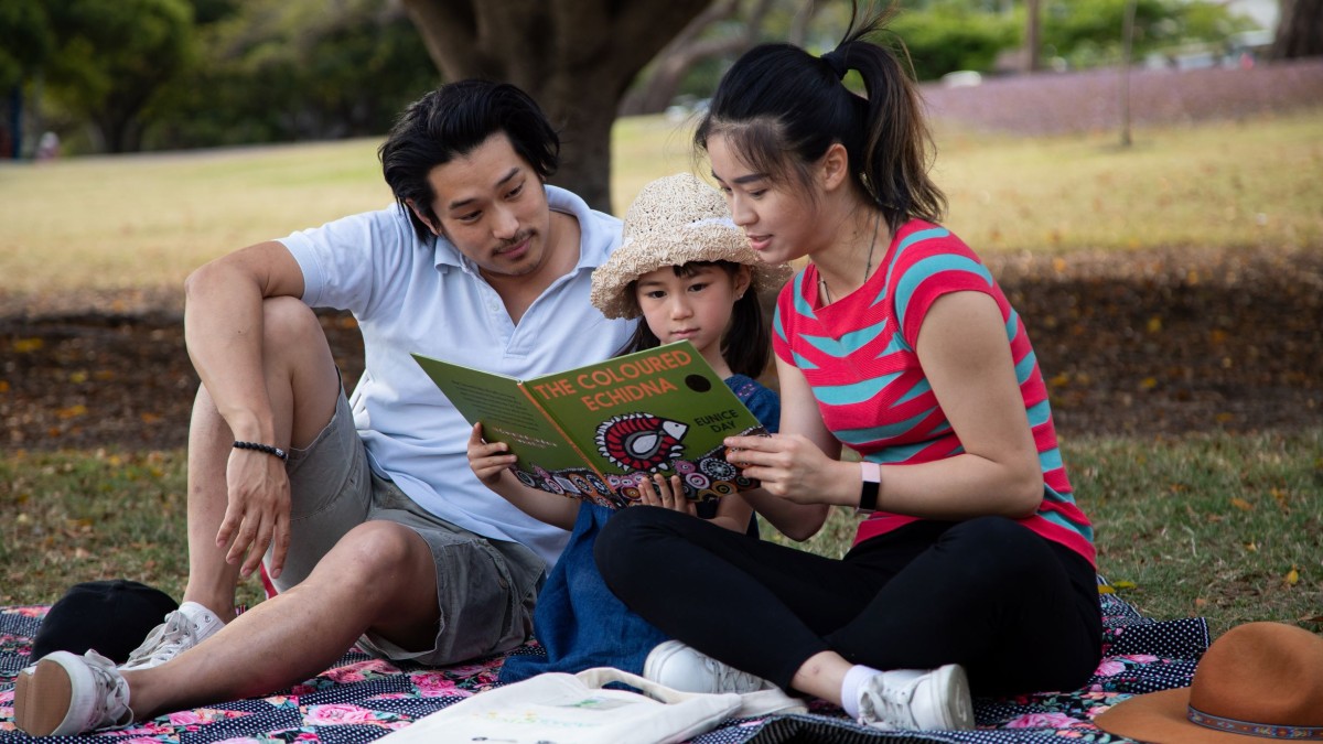Family in a park reading a picture book called The Coloured Echidna