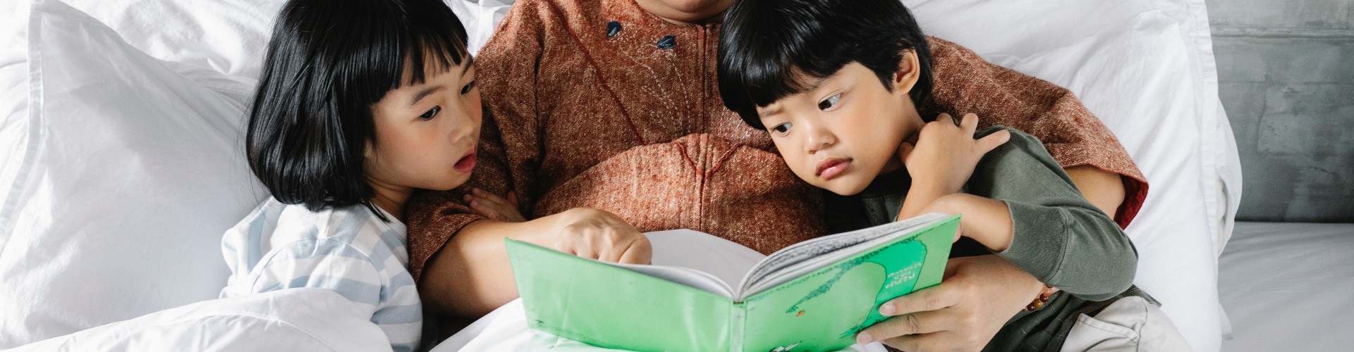 Lady reading a book with 2 children in bed