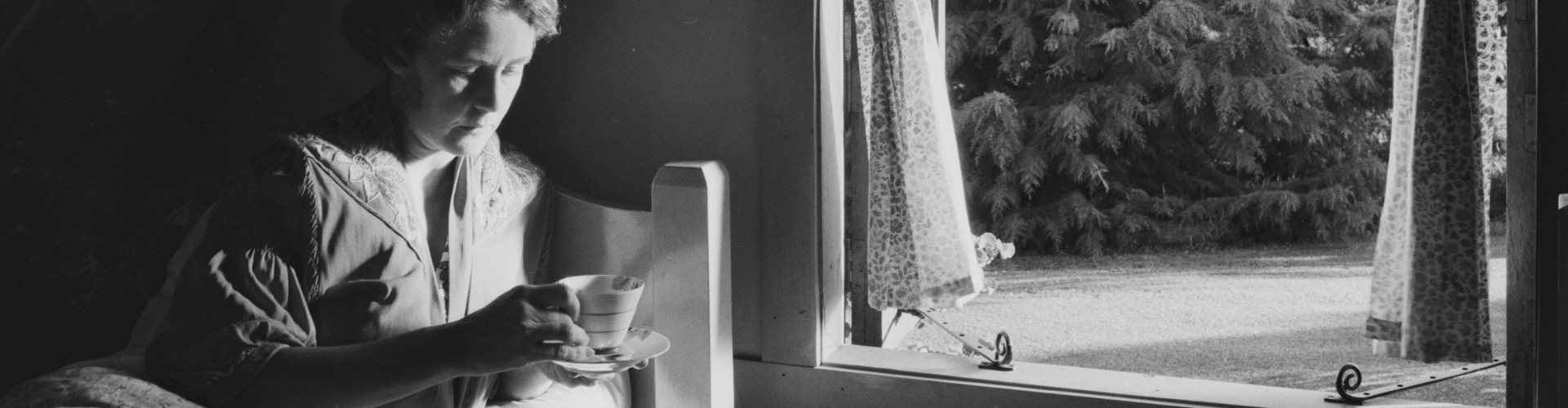 Woman lying in bed with a cup of tea at the High Tor guesthouse