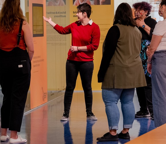 Showcase curator gestures to items behind glass in the Sovereign Stories showcase at State Library in front of a group of visitors.
