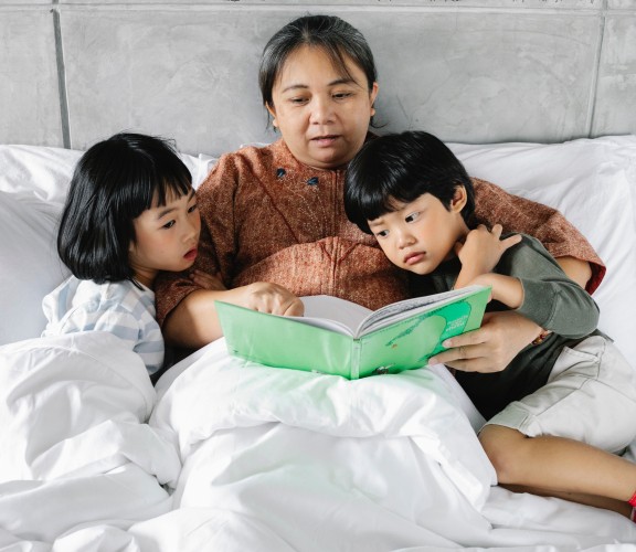 Lady reading a book with 2 children in bed