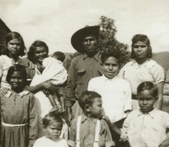 First Nations family outside wood building.