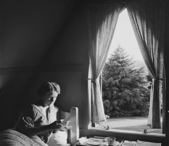 Woman lying in bed with a cup of tea at the High Tor guesthouse