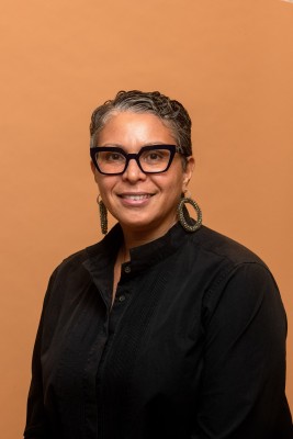 Photo of Cheryl Leavy against an orange background. Cheryl wears glasses and a black shirt.