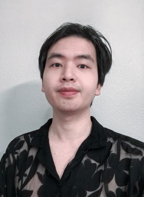 A photo of Gavin Yuan Gao who wears a black patterned shirt and stands against a white wall