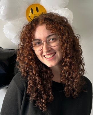 Lillian Telford smiles in front of a balloon in the shape of a flower and one in the shape of a black star