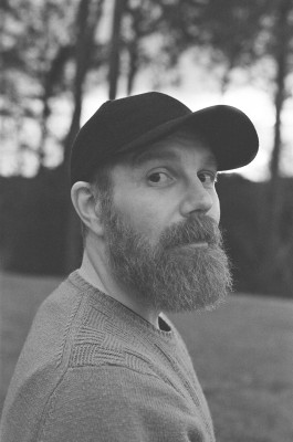 A black and white photo of Jarad Bruinstroop who is wearing a jumper and cap against a background of trees