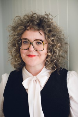 Photo of Sarah Kanake who wears glasses, a white blouse and a black vest