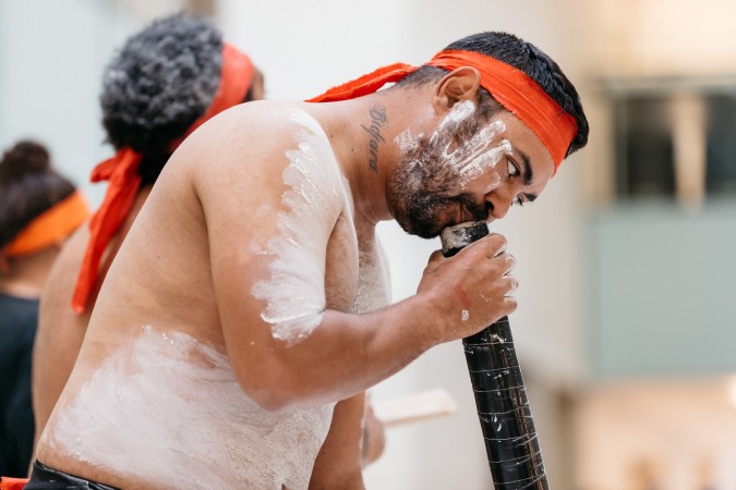 Nunukul Yuggera Dancers. A man painted in white clay plays a didgeridoo.