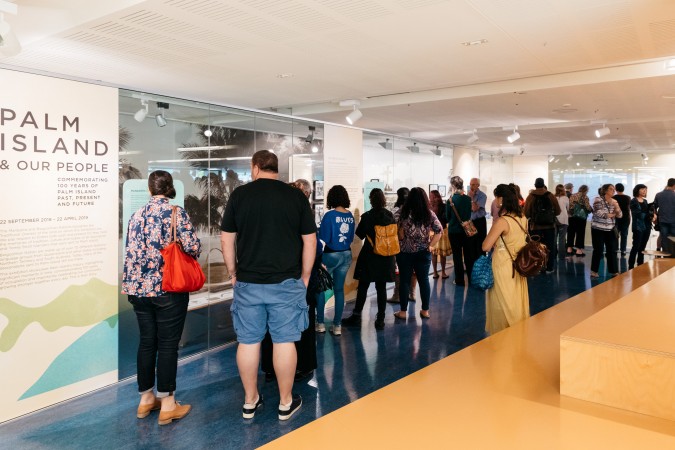 Palm Island and Our People Exhibition Launch. A group of about 20-30 people walk through a State Library exhibition.