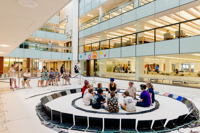 children and adults sitting in ring of keyboards and laptops