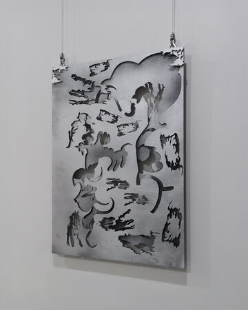 A close up photo of a grey spray painted laser cut piece of wood that has being layed. Is seen in front of a white background and is hanging on two hooks.