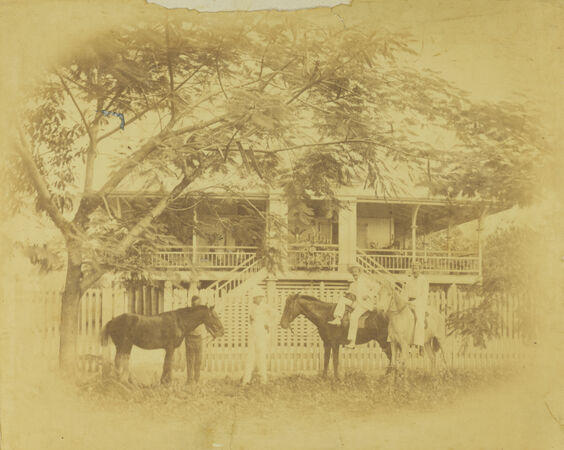 Four men and three horses. Two of the horses with riders sitting on them. In front of a two storey house in Cairns.