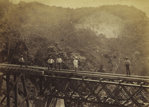Five men on a bridge across the Stoney Creek Valley, with the railway crossing the Red Bluff cliff in the background.
