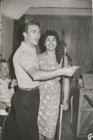 Black and white image of young man clicking fingers and woman smiling behind microphone