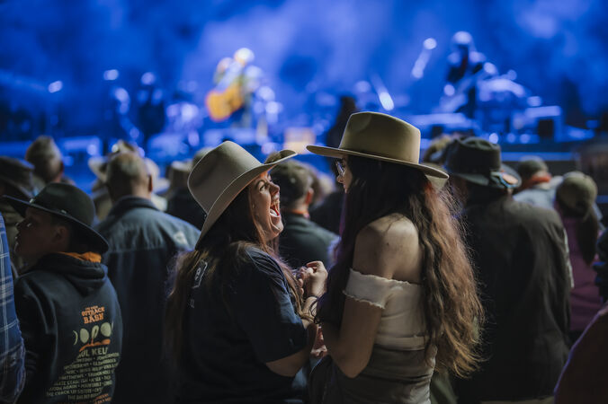 Two women in cowboy hats laughing in front of concert stage
